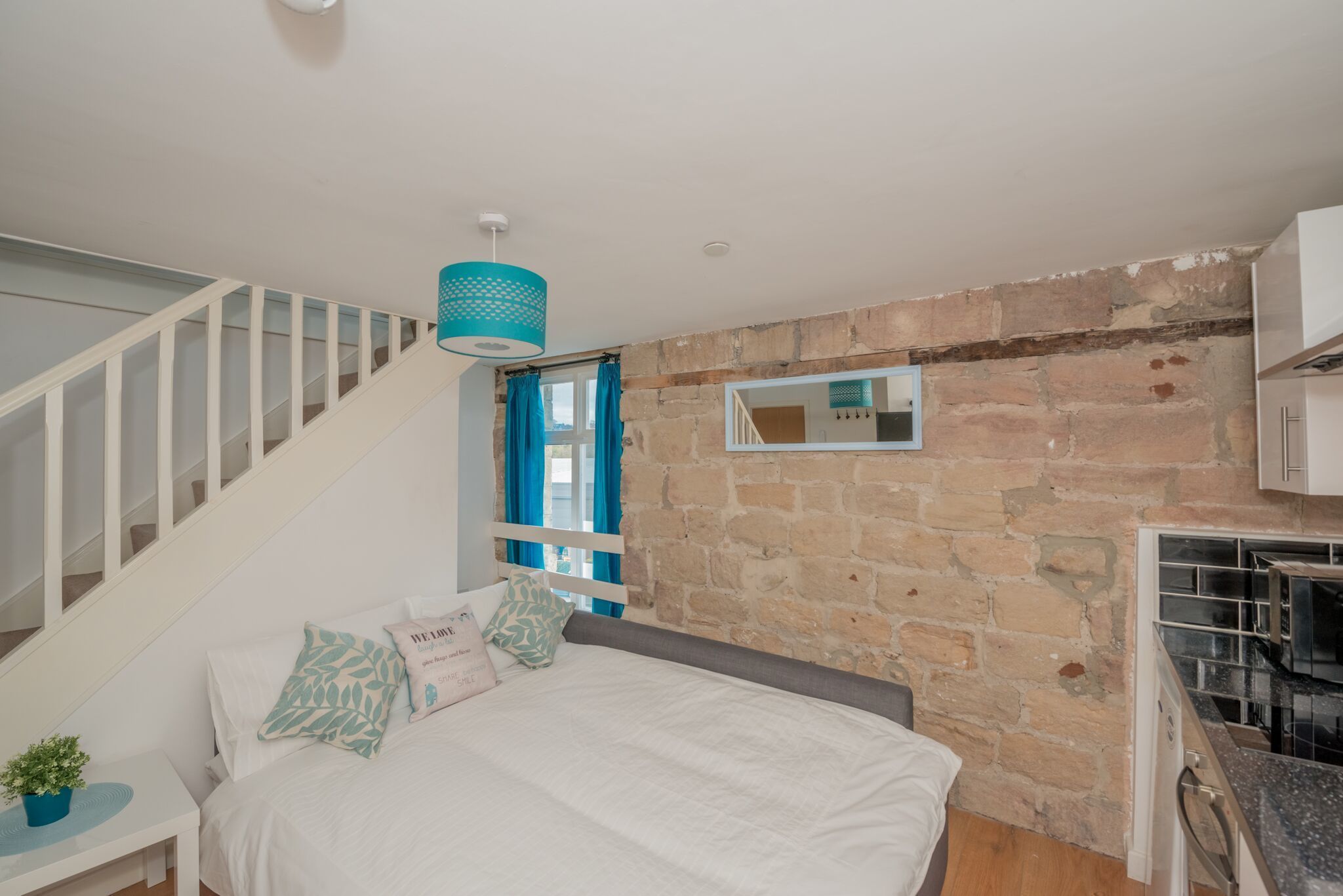 A bedroom with a bed, a staircase, a stone wall, and a kitchen area.