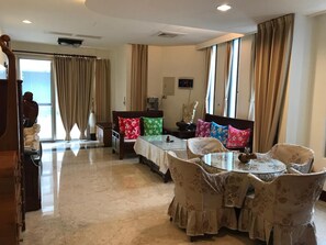 A hotel room with a dining area, a bed with floral pillows, a large window with curtains, and a view of the sea. - Guoguang B&B (Hualien City)