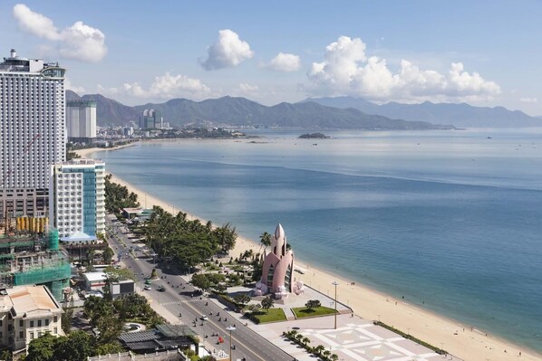 A coastal cityscape with a prominent hotel, a beach, and mountains in the background.