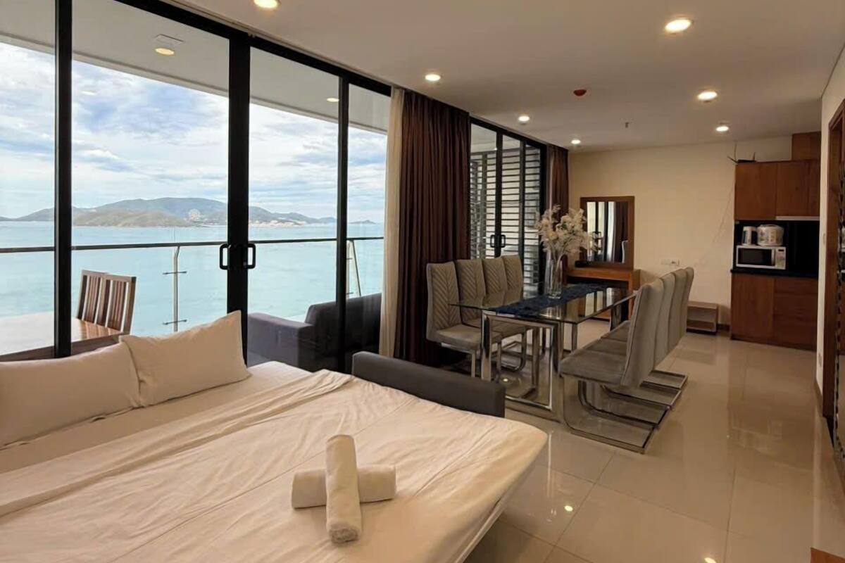 Une chambre d’hôtel moderne dotée d’un grand lit, d’un coin repas et offrant une vue sur la mer.