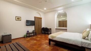 A bedroom with a bed, a desk, a chair, a TV, and a ceiling fan.