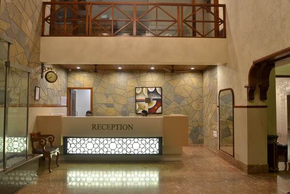 A reception area with a 'RECEPTION' sign, a clock, and a modern art piece on the wall. - Zaras Resort (Mawal)
