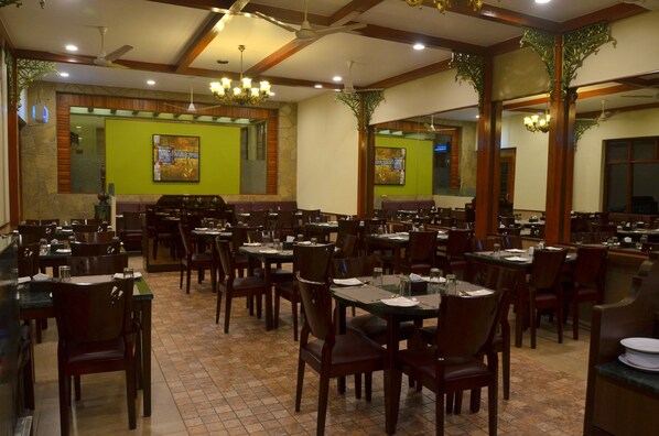 Un restaurant spacieux doté de nombreuses tables et chaises, de hauts plafonds avec des poutres en bois et d’œuvres d’art décoratives sur les murs.