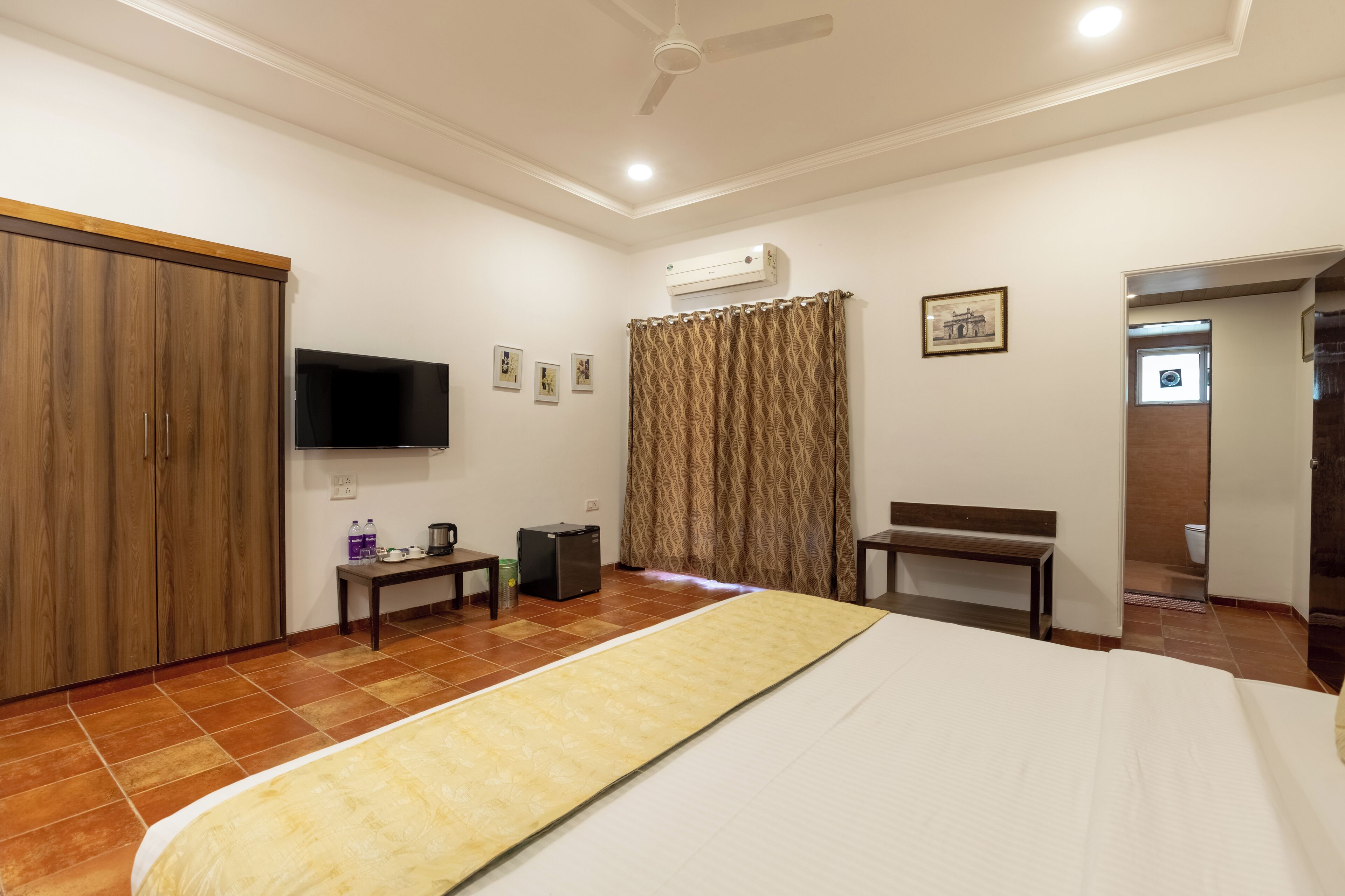 A hotel room with a bed, a television, a wardrobe, a desk, and an air conditioning unit.