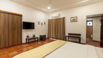 A hotel room with a bed, a television, a wardrobe, a desk, and an air conditioning unit.