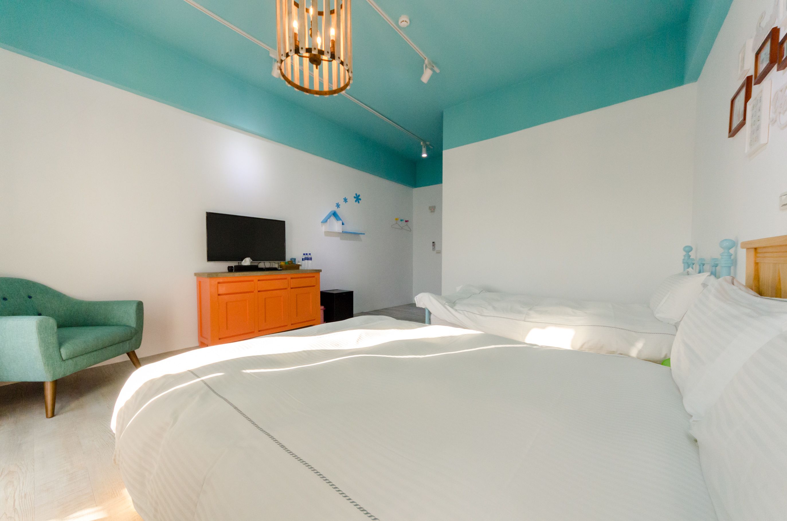 Un dormitorio con una cama, un televisor sobre un mueble, un aparador naranja y una silla verde.