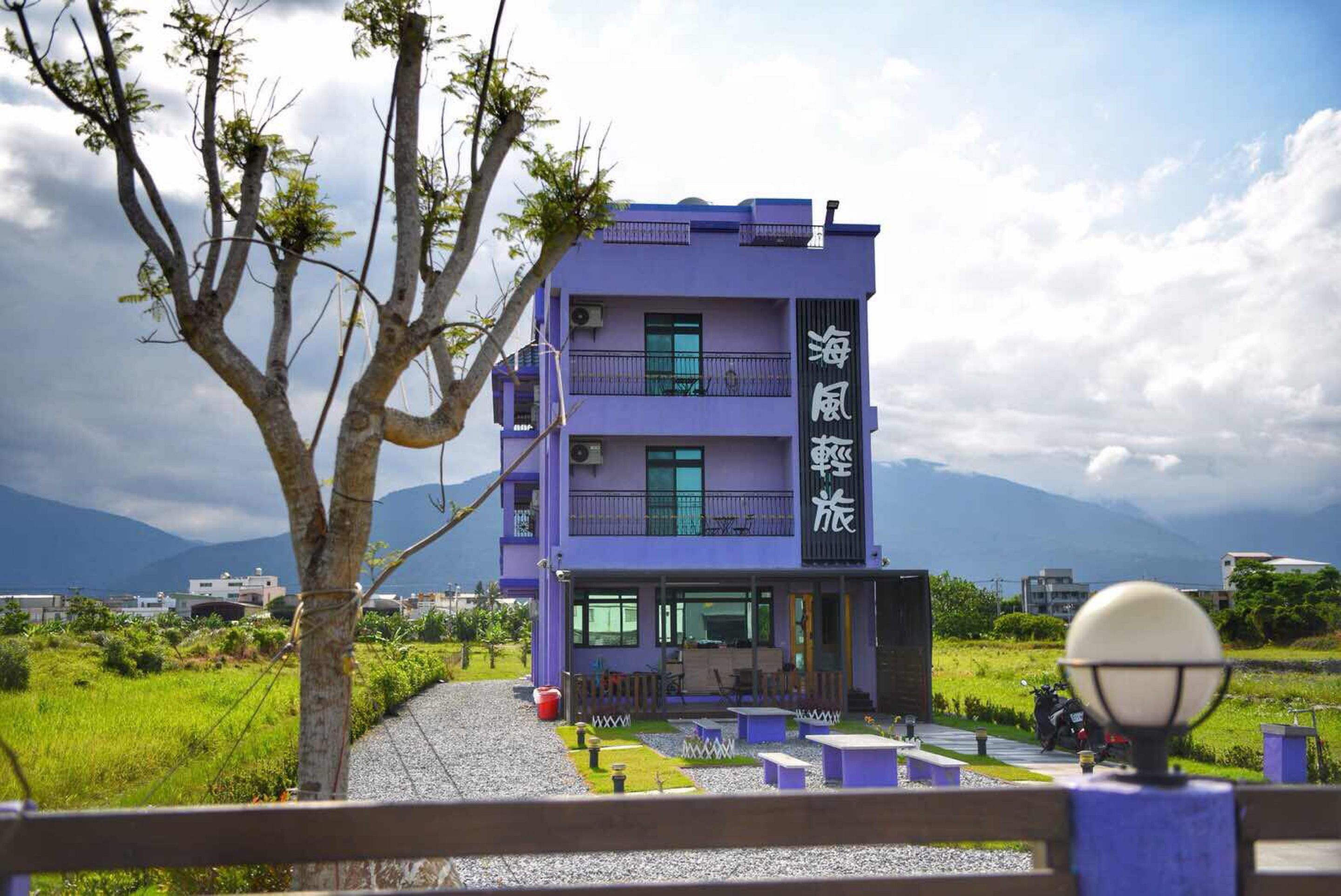 A multi-story building with a purple facade, outdoor seating area, and a view of mountains in the background.