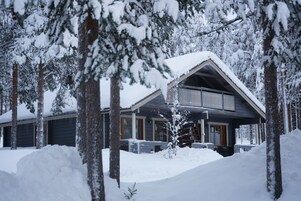 Uma cabana com varanda coberta, rodeada por árvores cobertas de neve.