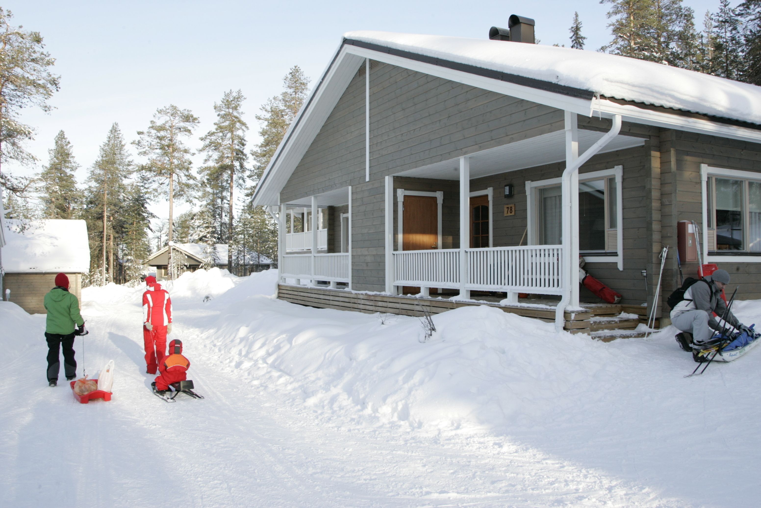 Una casa con porche, rodeada de nieve y árboles.