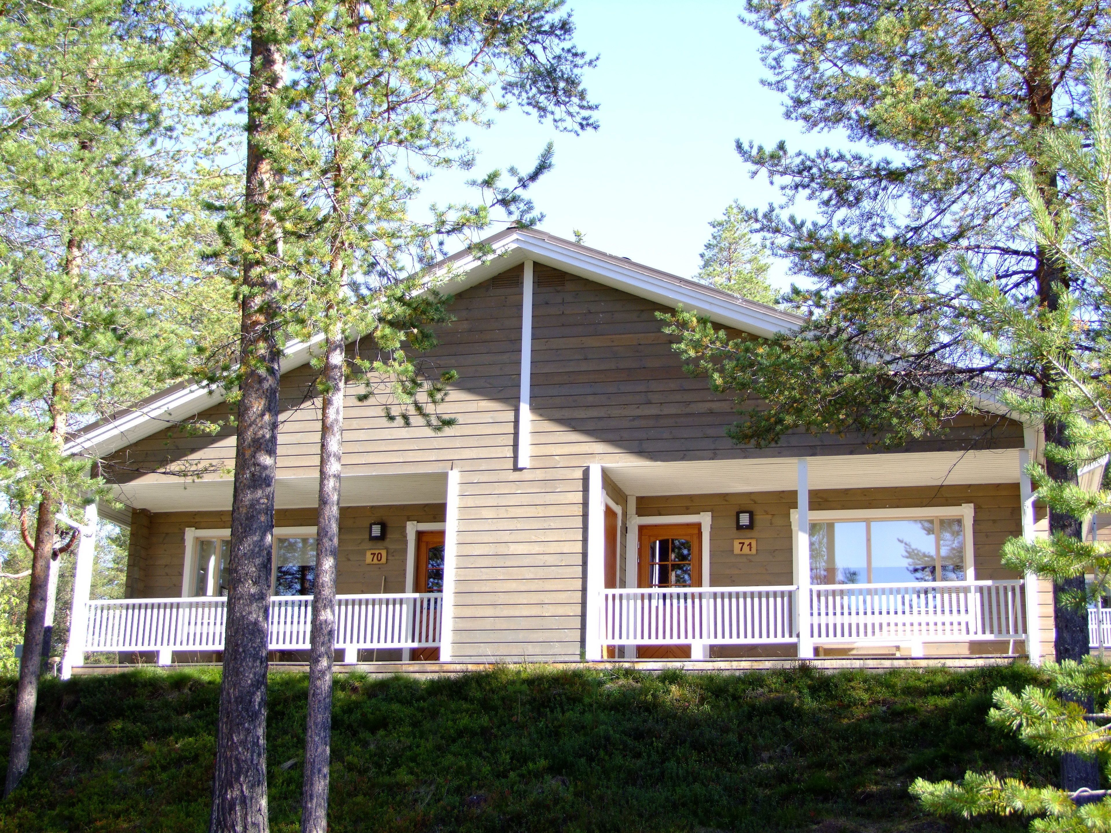 A two-story cabin with a porch, surrounded by pine trees.