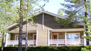 A two-story cabin with a porch, surrounded by pine trees.