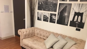 A beige tufted sofa with two pillows, a patterned rug, and a cityscape wall art collection. - Hanzhong House (Taipei)