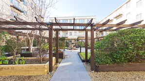 Un chemin menant à une pergola en bois, d’où l’on peut admirer un immeuble d’habitation.