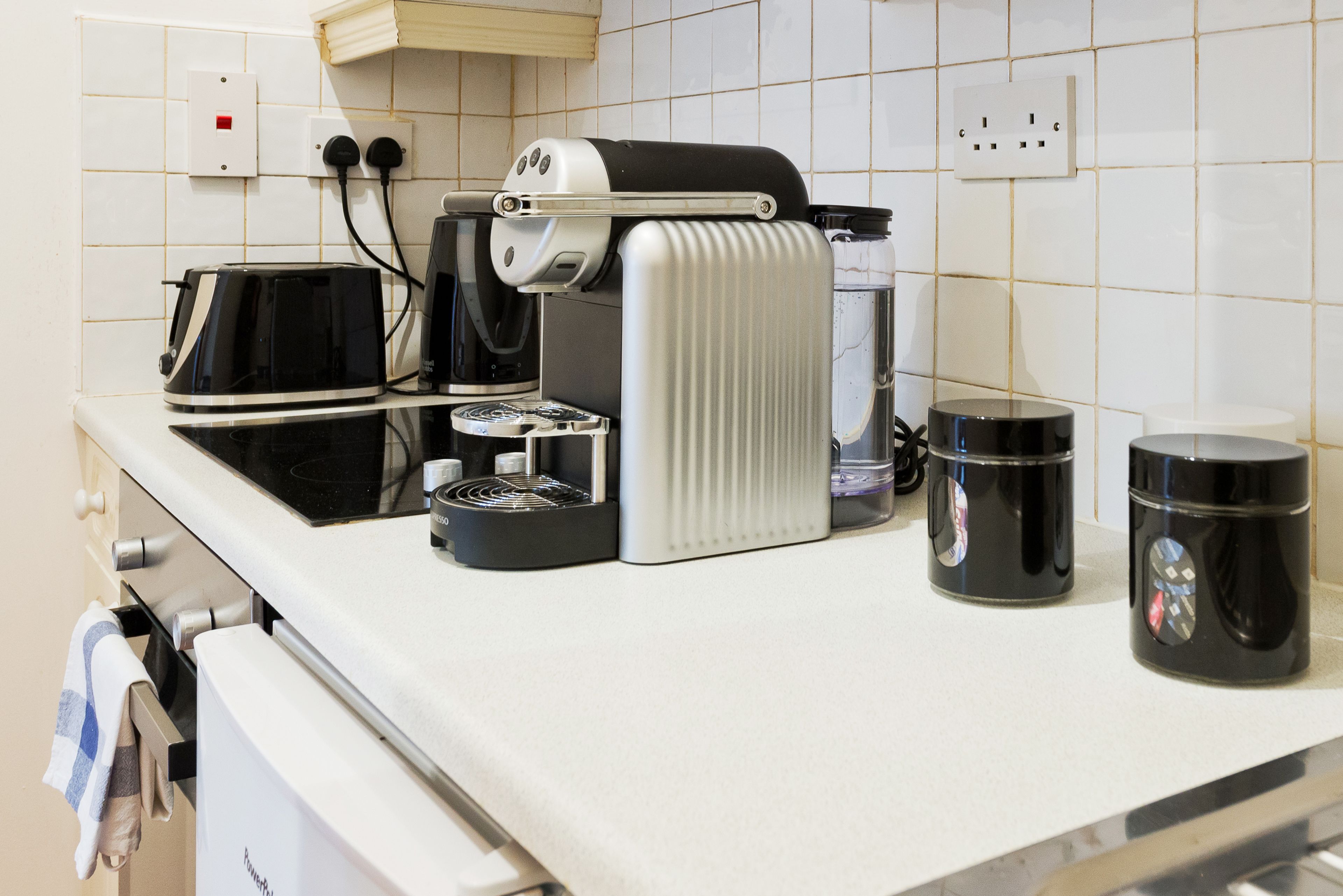 A kitchen with a coffee maker, toaster, and two black mugs on the counter.
