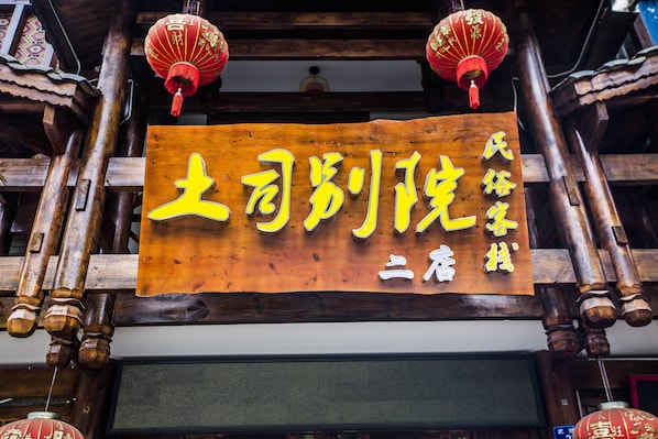 A wooden building with traditional Chinese architecture, including wooden beams and red lanterns. A sign with yellow characters is prominently displayed.