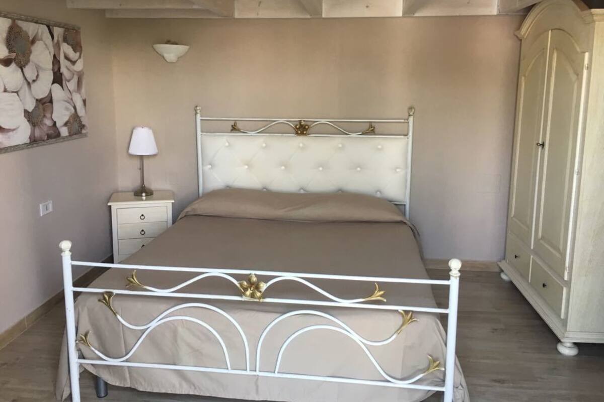 A bedroom with a bed, nightstand, lamp, wardrobe, and a decorative wall piece.