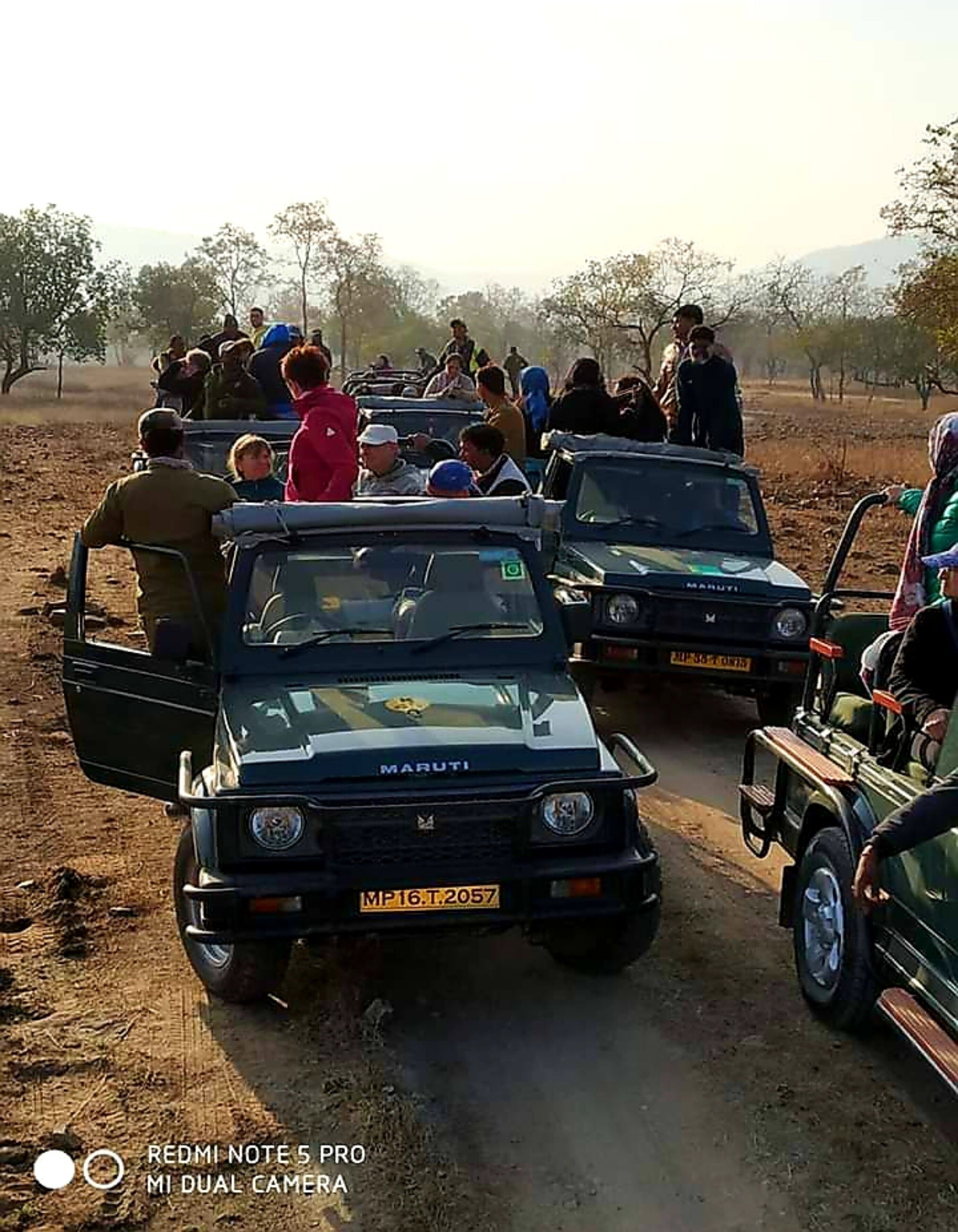 A group of people gathered around a Maruti vehicle on a dirt road.
