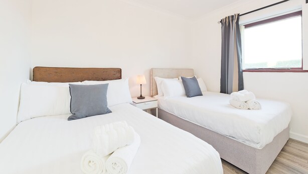 Una habitación de hotel con dos camas, una mesita de noche con lámpara y una ventana con cortinas.