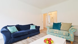 Una sala de estar con un sofá azul oscuro, un sillón estampado y una mesa de centro blanca con manzanas.