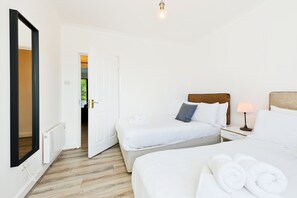A hotel room with two beds, a bedside table with a lamp, and a large mirror.
