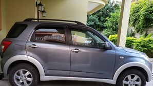 A compact SUV parked in front of a building with a covered entrance and a garden area. - Keep Cool Apartment (Gros Islet)