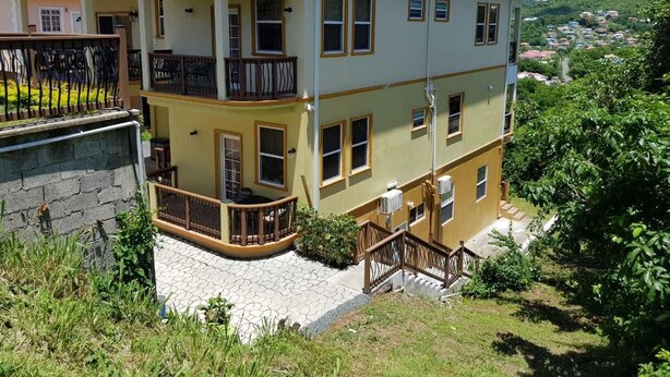A two-story building with balconies, a stone pathway, and a view of a hillside. - Keep Cool Apartment (Gros Islet)