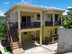 A two-story house with a balcony on the upper floor, a staircase leading to the upper level, and a small outdoor area with a concrete floor. - Keep Cool Apartment (Gros Islet)