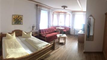 A room with a bed, a red sofa, a small table, a mirror, and a window with curtains.