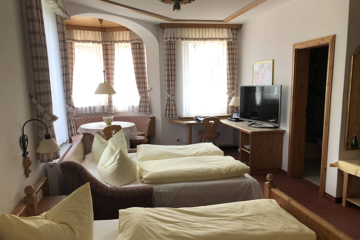A hotel room with two beds, a desk with a television, a dining table, and a window with curtains.