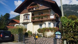 A two-story building with balconies adorned with flowers, a sign indicating a restaurant, and a mountain backdrop. - Gästehaus Maria (Garmisch-Partenkirchen)