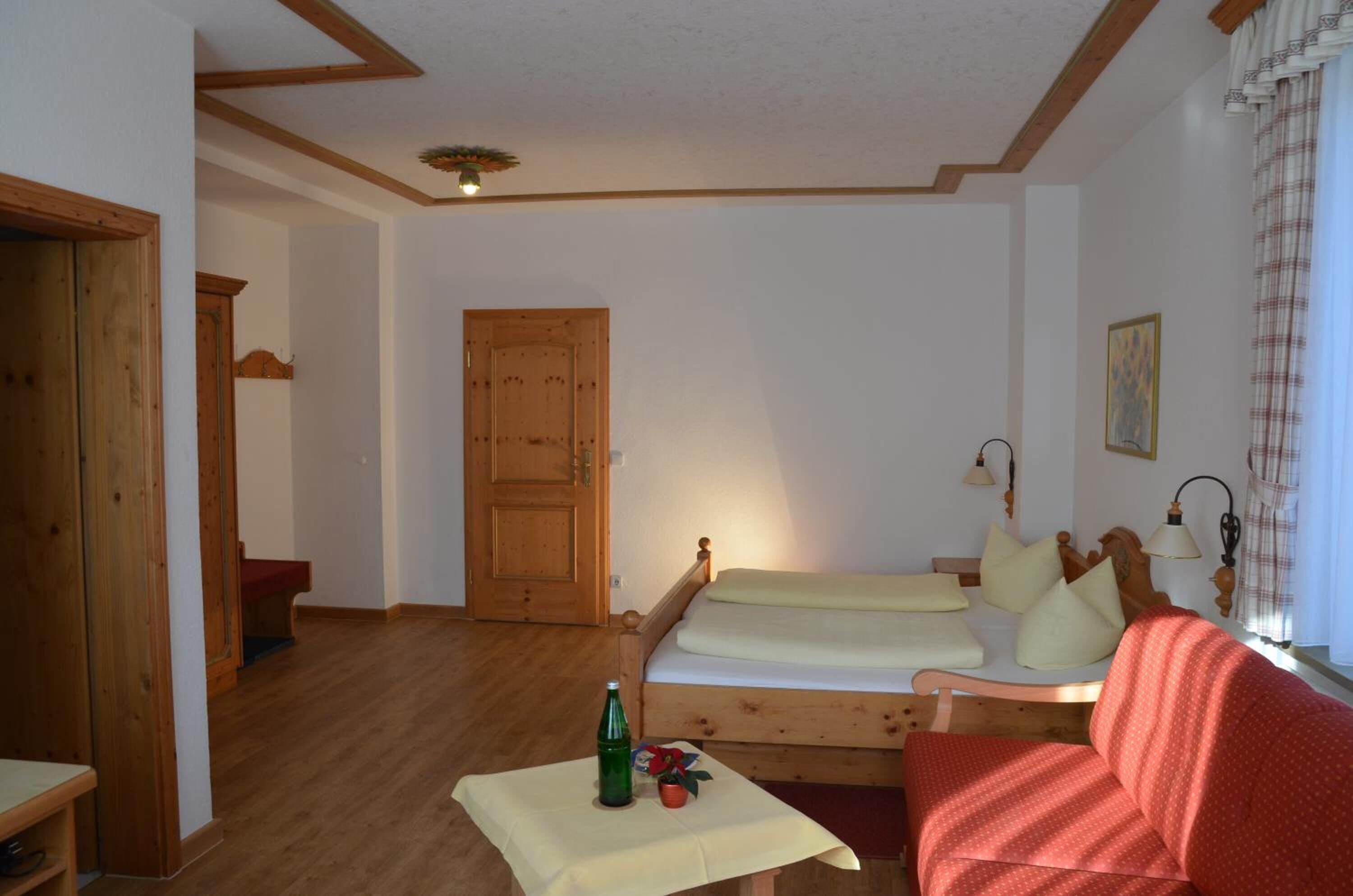 A cozy room with a wooden bed, a small table with a bottle, and a red sofa.