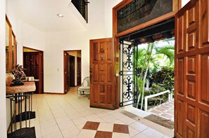 A spacious hallway with wooden doors, a tiled floor, and a view of a lush garden outside.