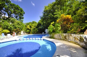 A swimming pool with blue water, surrounded by lush greenery and a stone wall.