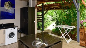 A compact kitchen with a washing machine, a small table with a glass cover, and a view of lush greenery. - Redoute Paradise (Fort-de-France)