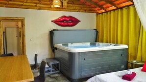 A room with a wooden ceiling, a hot tub, a bed with a white cover, a table with chairs, and a yellow curtain. - Redoute Paradise (Fort-de-France)