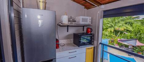 A compact kitchen with a refrigerator, microwave, and a small shelf with a coffee maker.