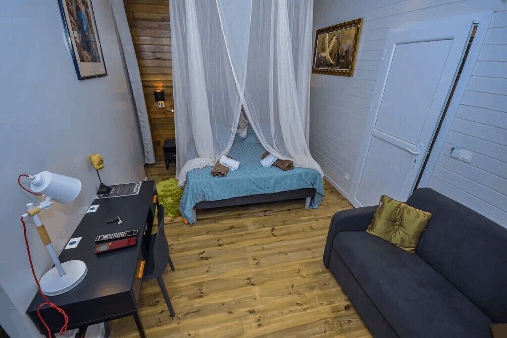 Habitación pequeña con cama, escritorio con lámpara, sofá y una puerta.