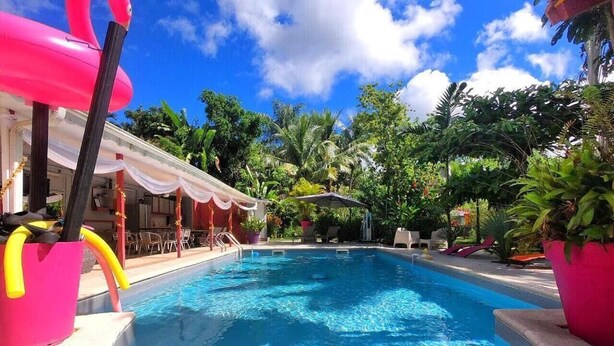 A swimming pool with a clear blue water surface, surrounded by lush greenery and a covered area with white canopies. - Redoute Paradise (Fort-de-France)