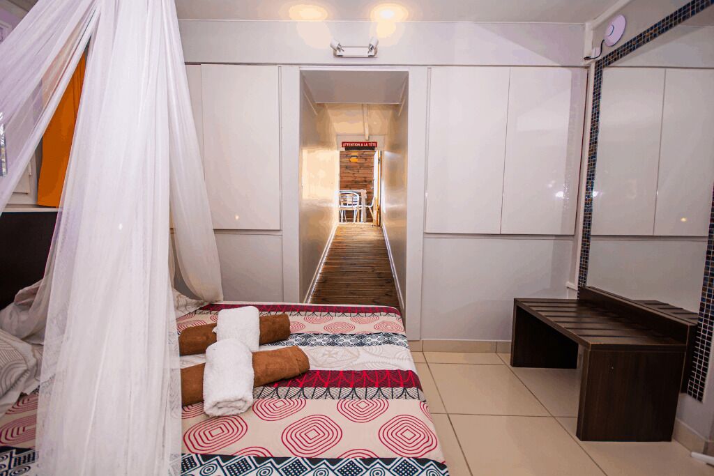 Un dormitorio con cama, una mesita de noche, un banco, un espejo y un pasillo que lleva a un baño.