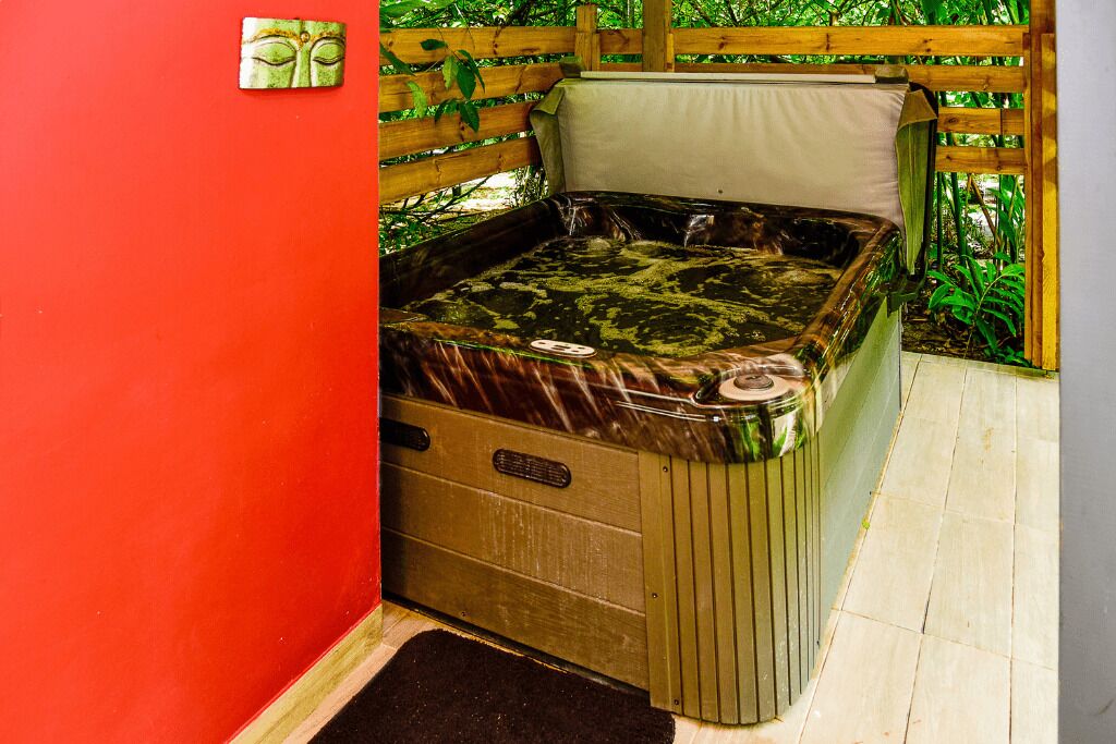 Uma banheira de hidromassagem com um banco de madeira, cercada por um portão de madeira e vegetação.