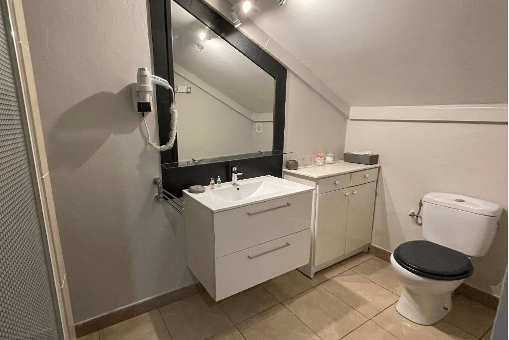 Un baño pequeño y moderno con un lavamanos blanco, un inodoro negro y un espejo grande sobre el lavamanos.