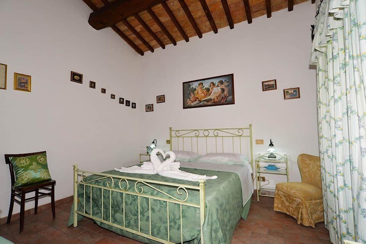 Ein Schlafzimmer mit Bett, Sessel, Nachttisch und einem Bild an der Wand.