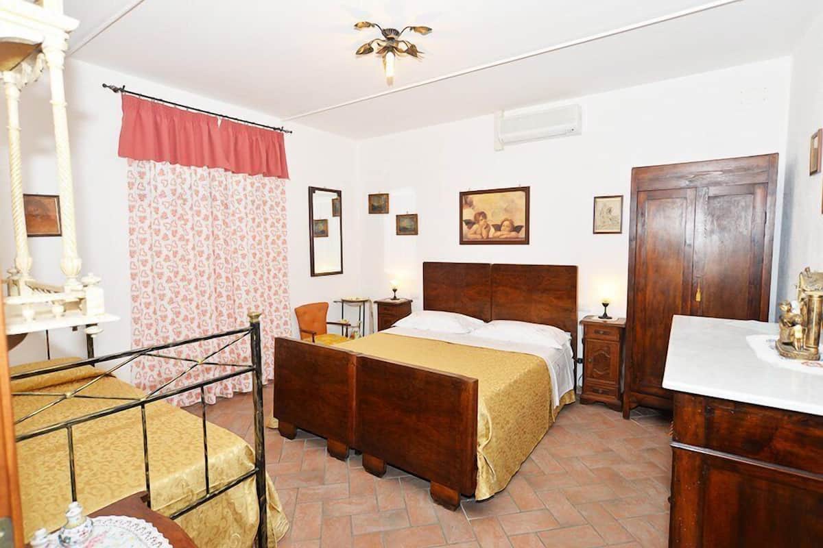 Ein Schlafzimmer mit einem hölzernen Bett, einem kleinen Nachttisch, einem Stuhl, einem Kleiderschrank und einem Spiegel an der Wand.