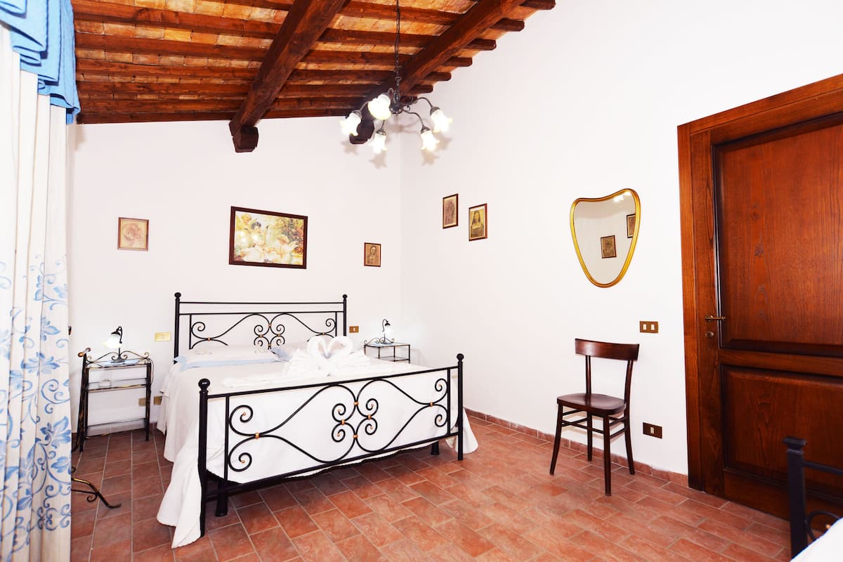 Ein Schlafzimmer mit einem Bett, einem Sessel, einer Holztür und einer Decke mit sichtbaren Balken.