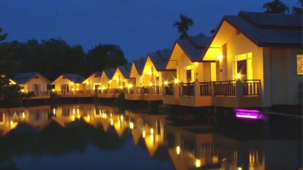 A row of bungalow-style accommodations with balconies, reflecting in a calm body of water. - Maerim Whale Park Resort (Mae Rim)