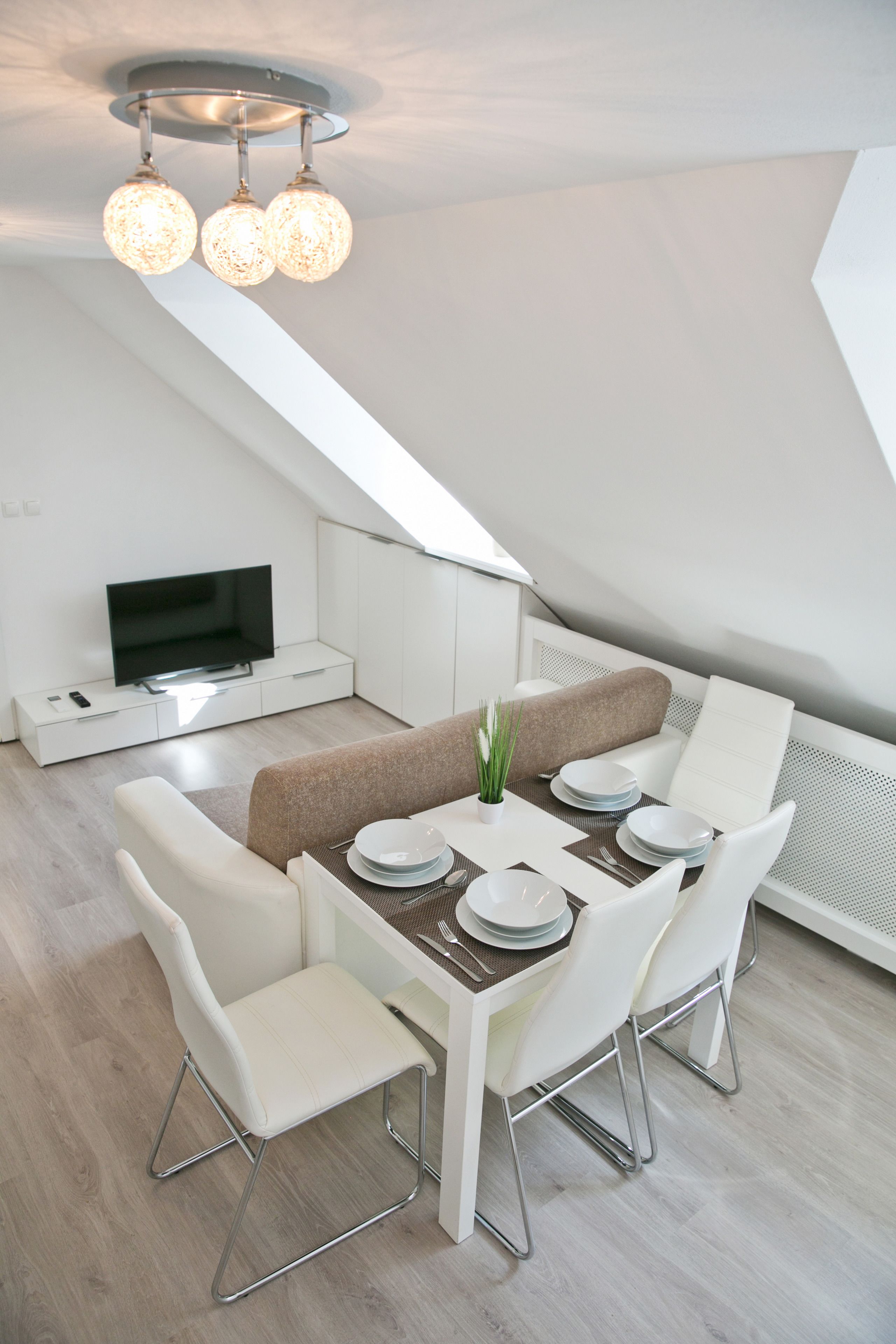 Un espace de salle à manger moderne avec une table dressée pour quatre personnes, des chaises blanches et un luminaire suspendu au plafond.