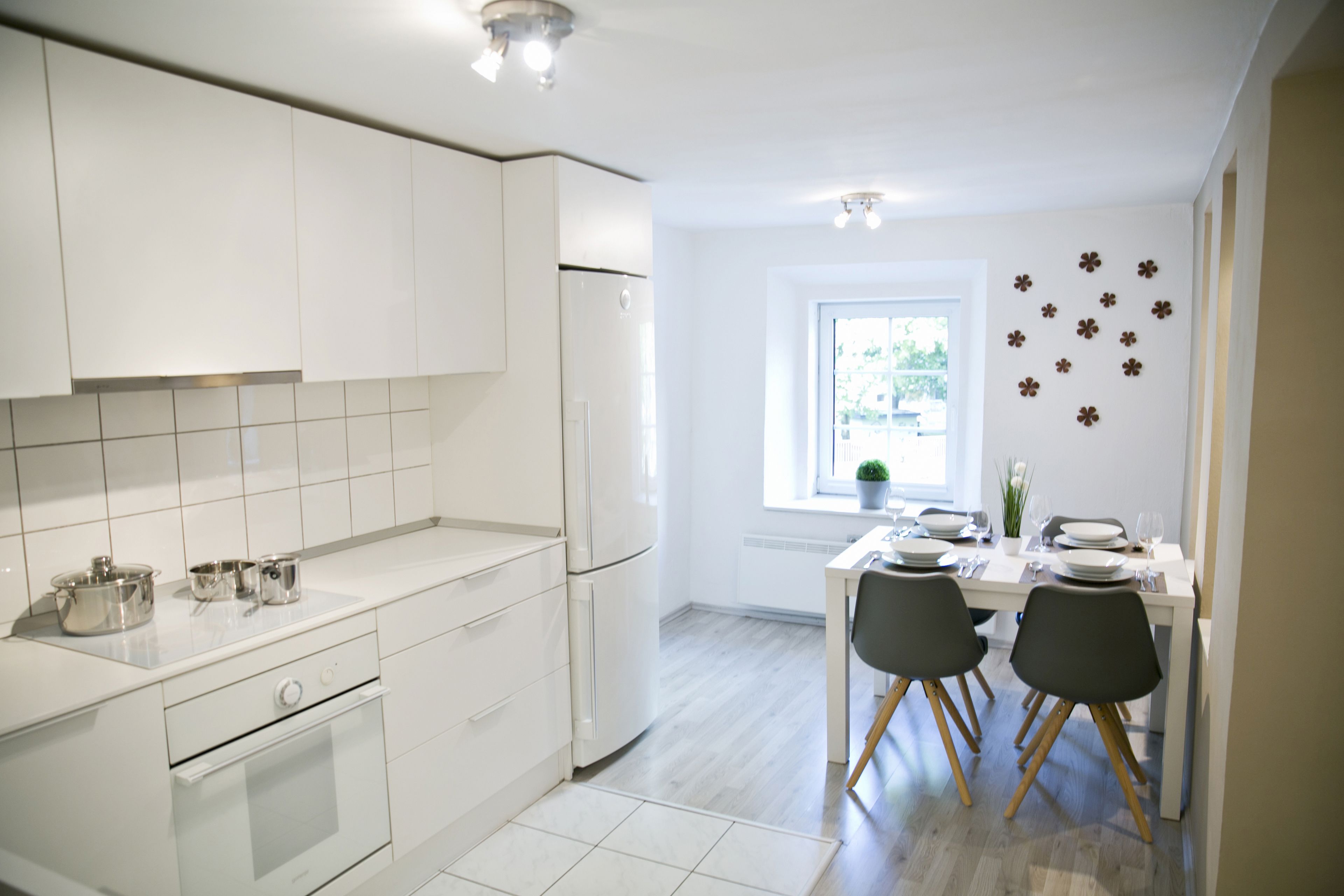 Een moderne keuken met witte kasten, een ingebouwde oven en een eethoek met twee stoelen en een tafel gedekt voor twee personen.