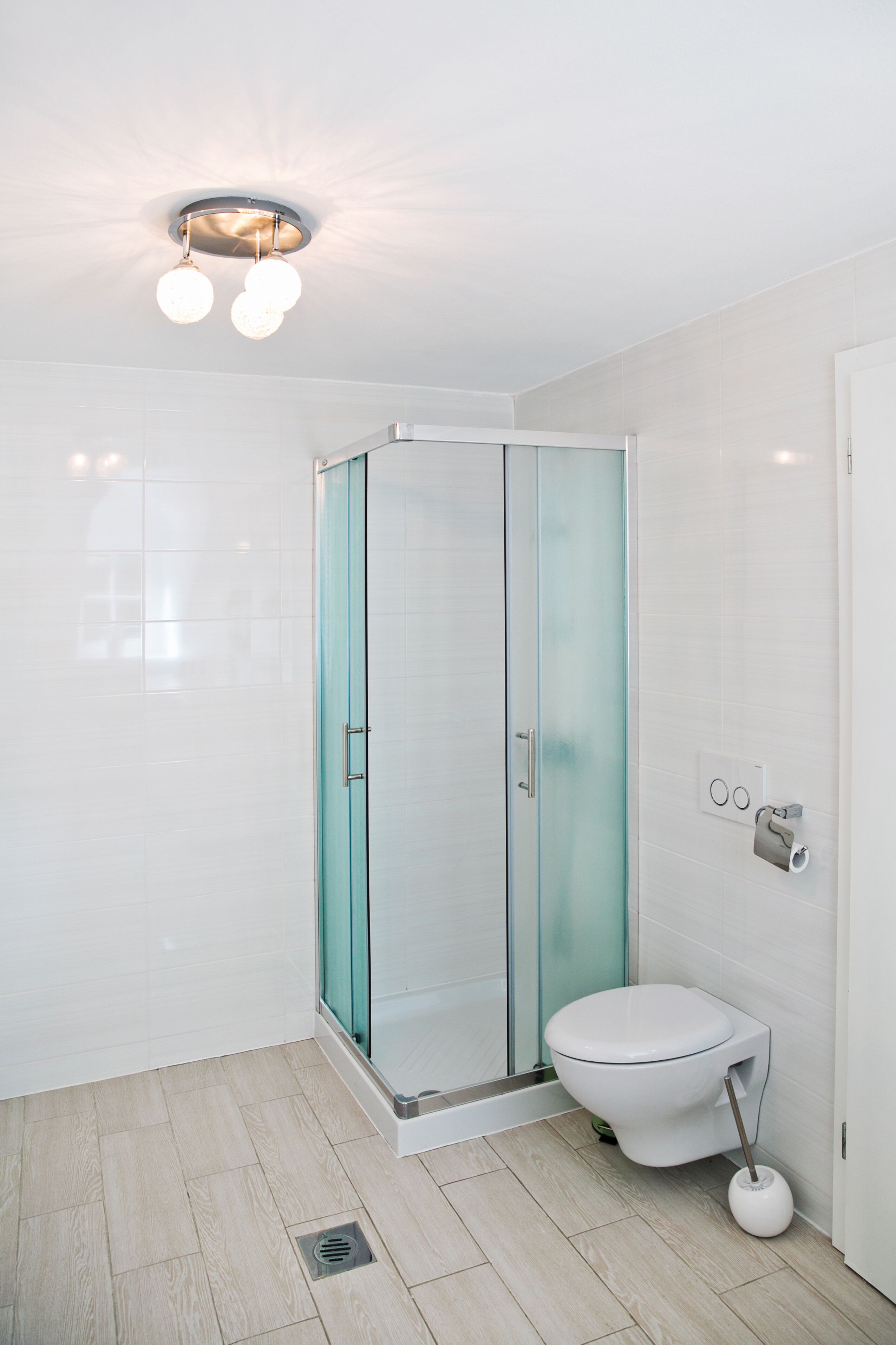 A modern bathroom with a glass shower enclosure, a white toilet, and a light fixture above the shower.