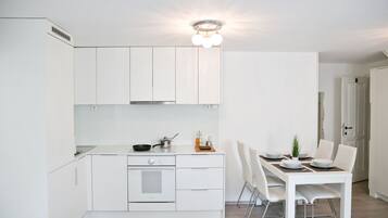 Una cocina moderna con armarios blancos, horno empotrado y comedor con mesa y sillas blancas.