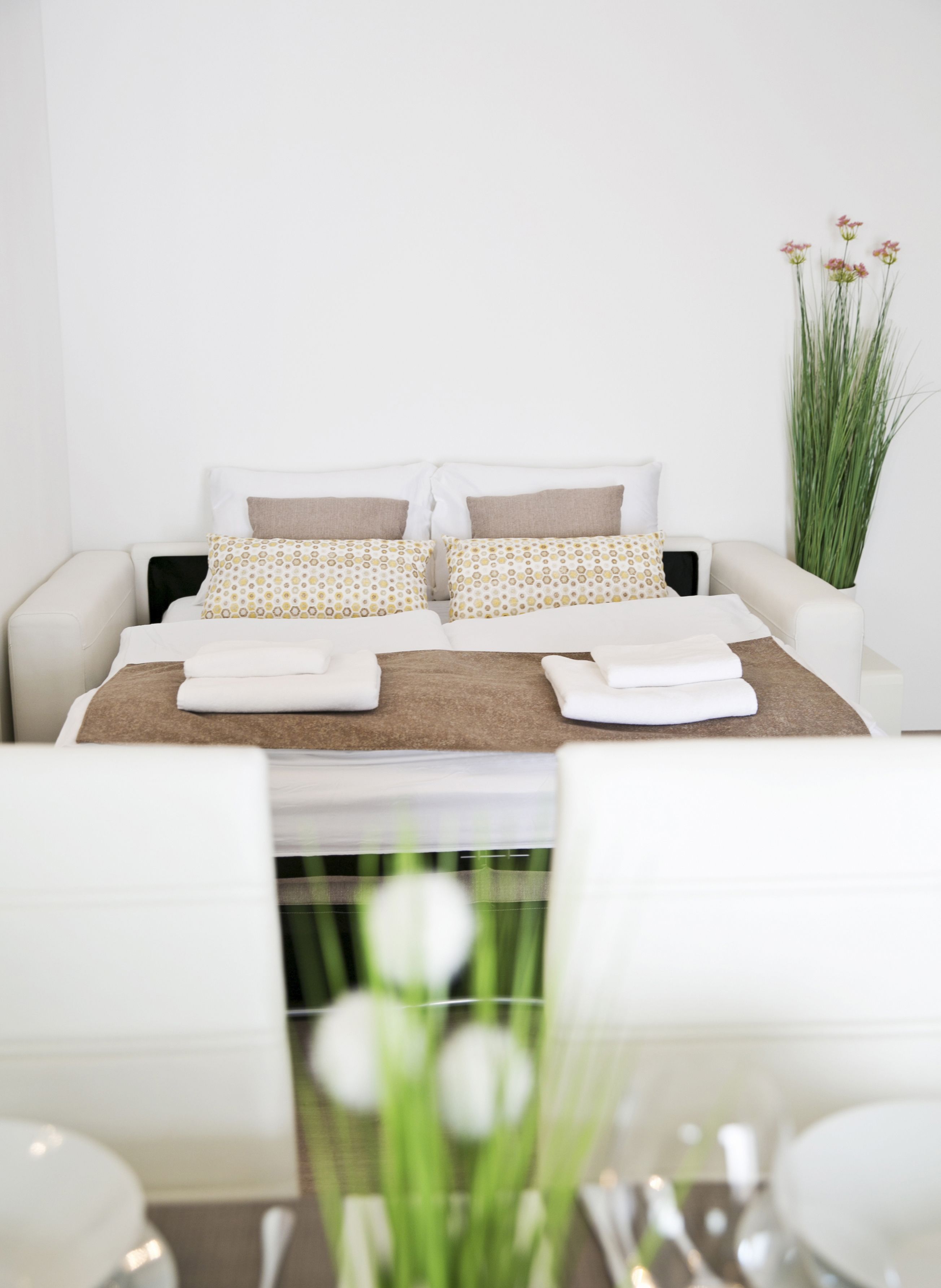 Une chambre à coucher bien rangée, avec un lit, des oreillers et une plante sur la table de chevet.
